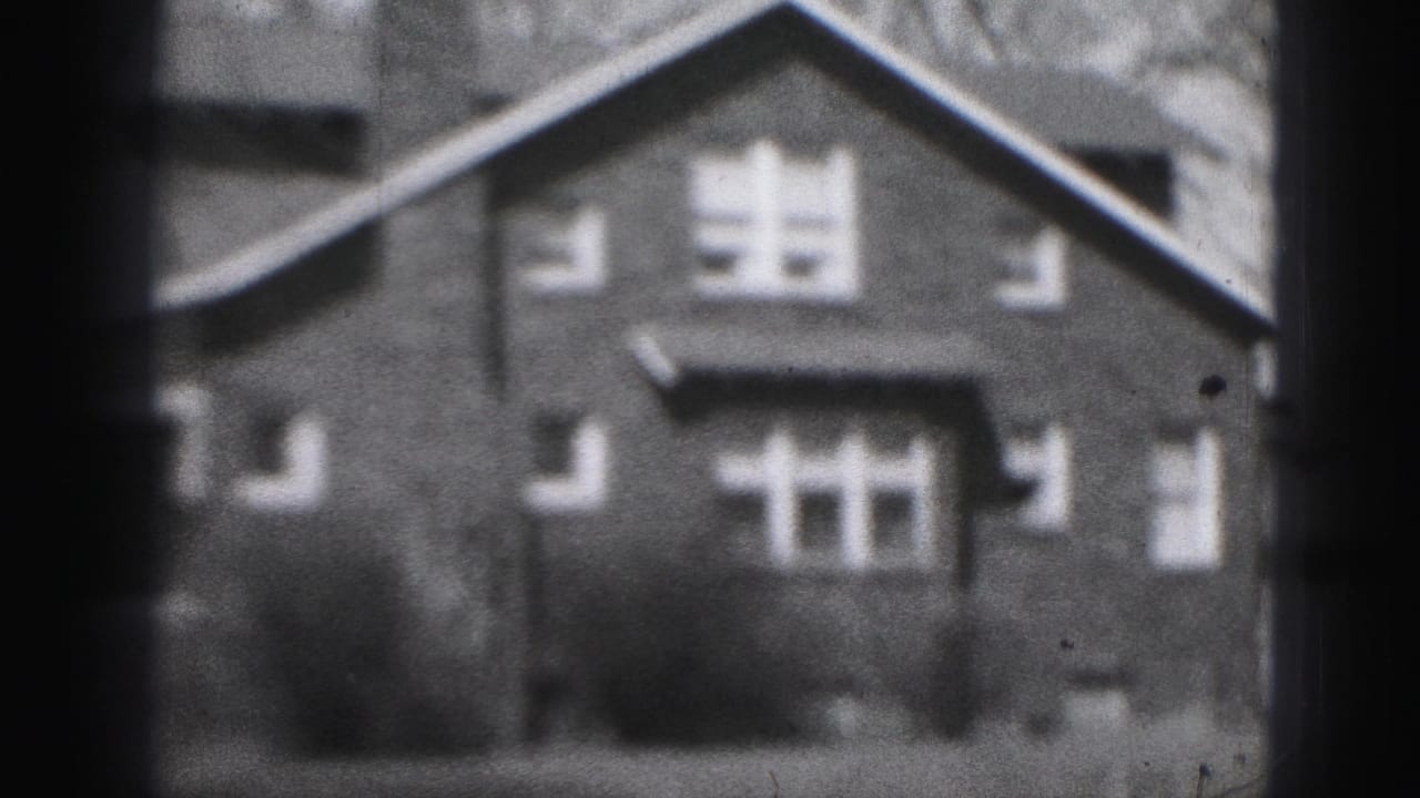 1975 Harrisburg home-movie frame showing the brick house facade, roofline, chimney, windows, and front shrubs.
