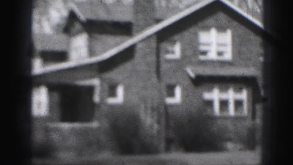 1975 Harrisburg 8mm frame with the brick house shifted in view, showing a porch area, windows, shrubs, and roofline.