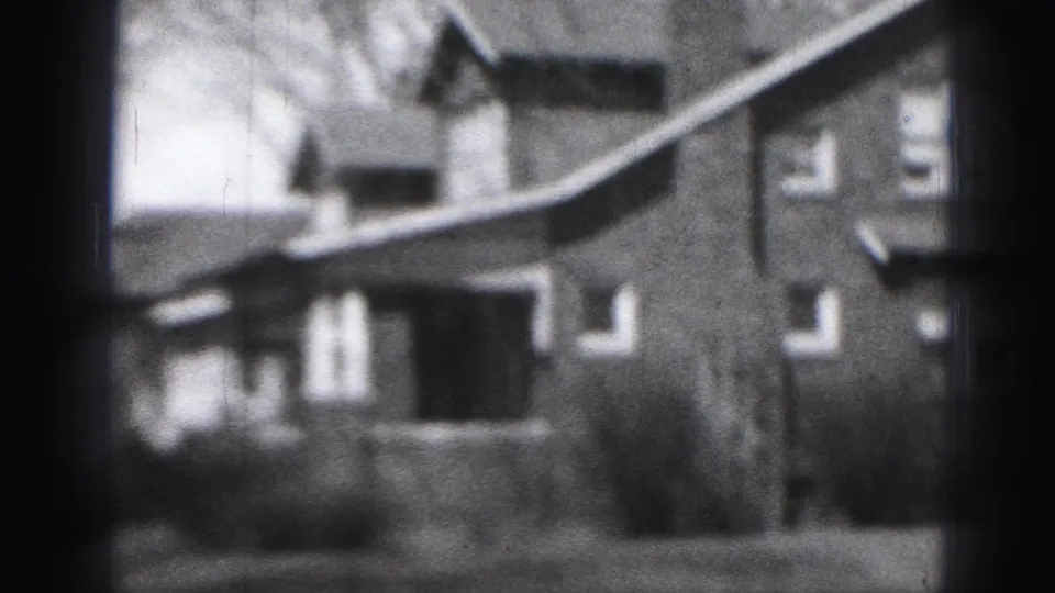 1975 Harrisburg home-movie frame near the end of the pan, with the brick house partly cropped by dark film borders.