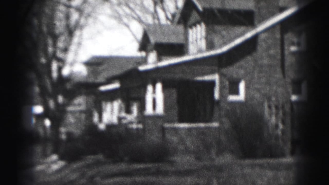1975 Harrisburg home-movie frame showing a large brick suburban house from a low outdoor angle with bare trees and lawn.