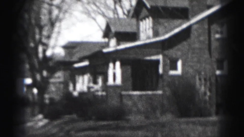 1975 Harrisburg home-movie frame showing a large brick suburban house from a low outdoor angle with bare trees and lawn.