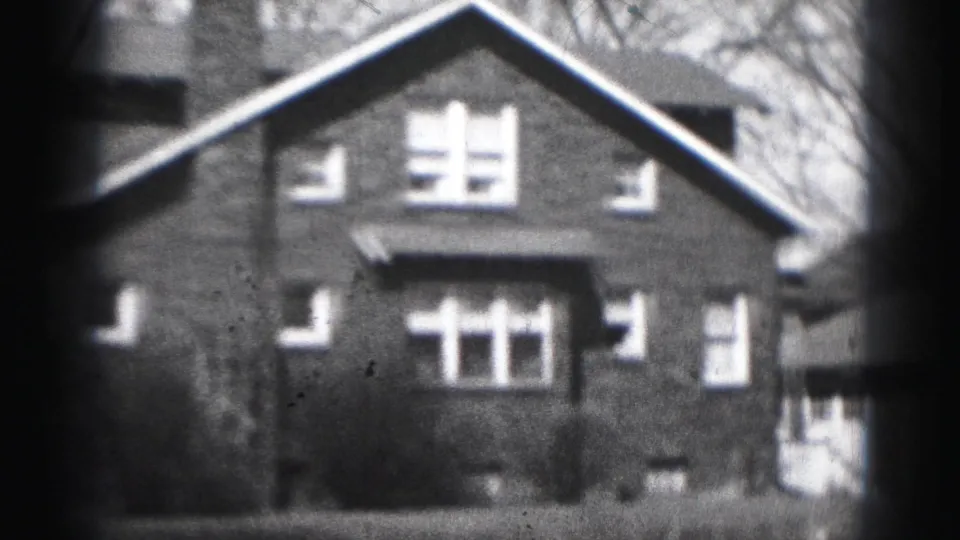 1975 Harrisburg home-movie frame with a closer view of the brick house front, roof peak, windows, lawn, and leafless trees.