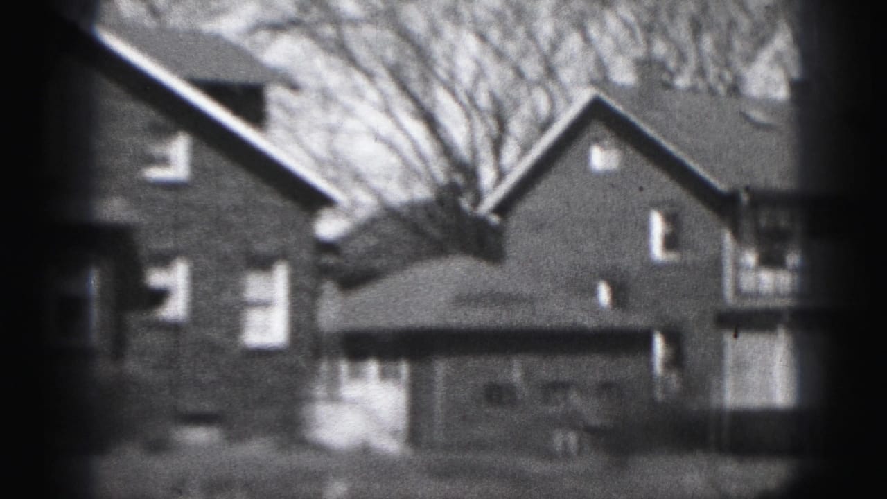 1975 Harrisburg 8mm frame showing brick residential houses, pitched roofs, white-trimmed windows, and bare tree branches.