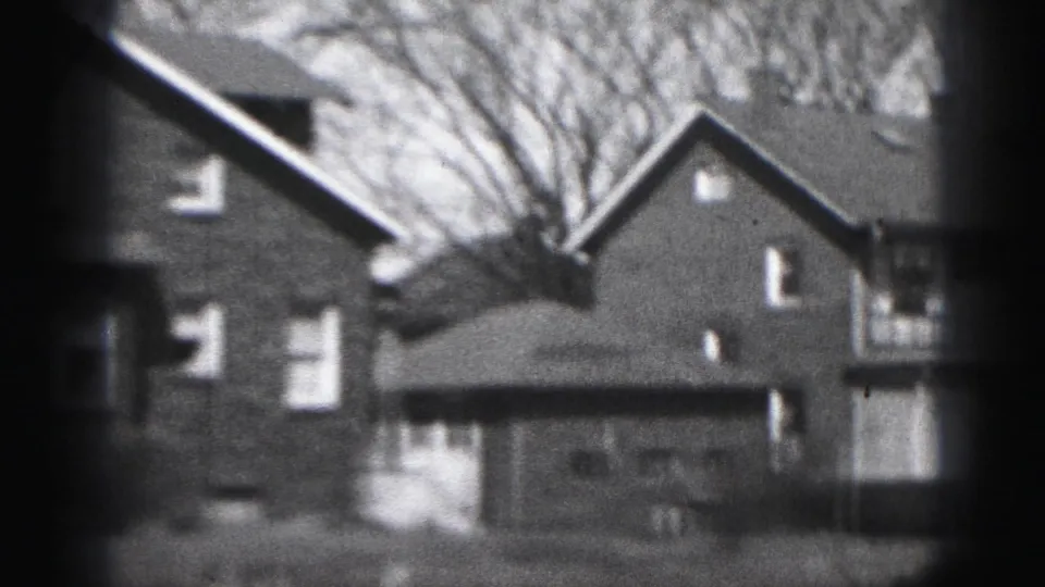 1975 Harrisburg 8mm frame showing brick residential houses, pitched roofs, white-trimmed windows, and bare tree branches.