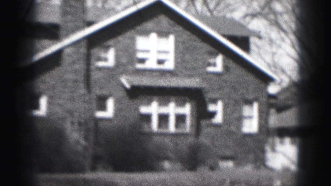 1975 Harrisburg home-movie frame showing the front of a two-story brick residential house with white trim and bare branches.