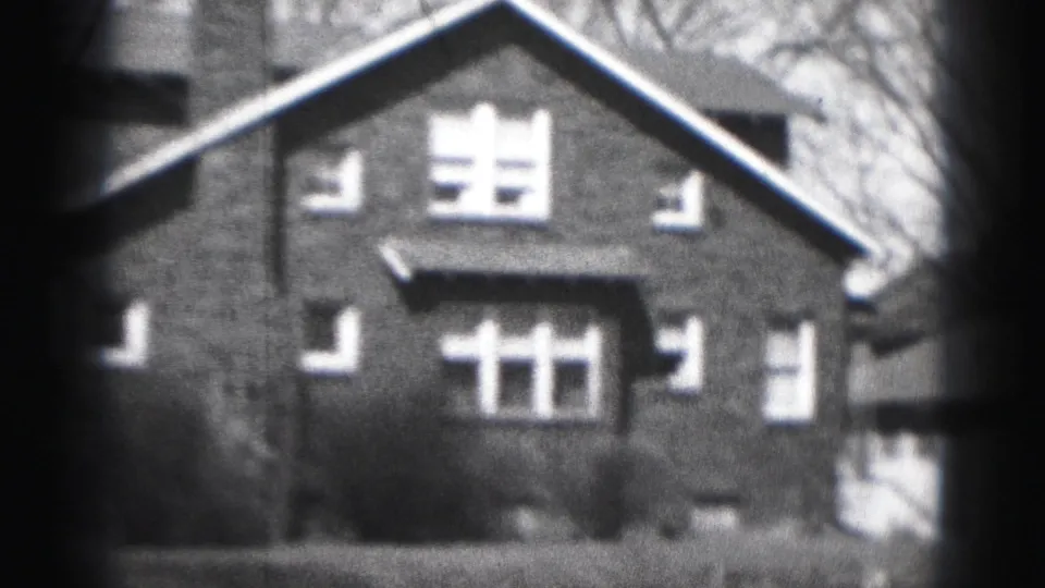 1975 Harrisburg home-movie frame showing the front of a two-story brick residential house with white trim and bare branches.