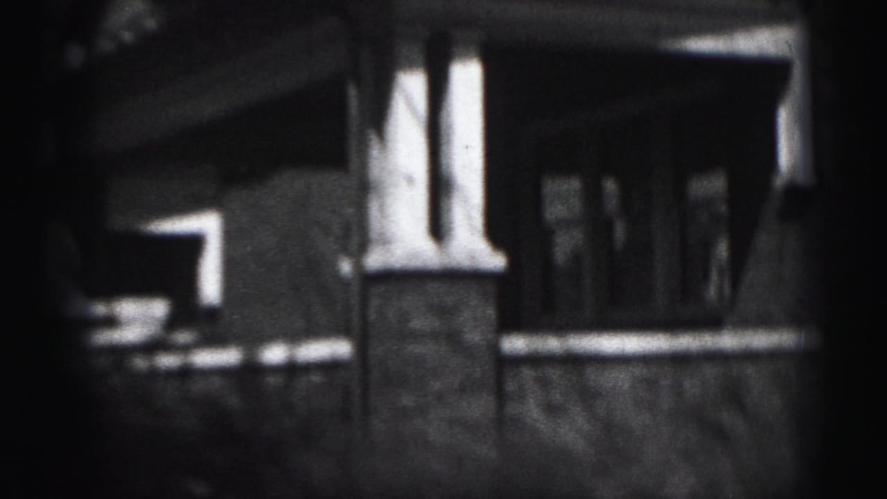 Close exterior view of a covered porch on the Harrisburg brick house, with columns, shadowed entry, and a low wall or railing.