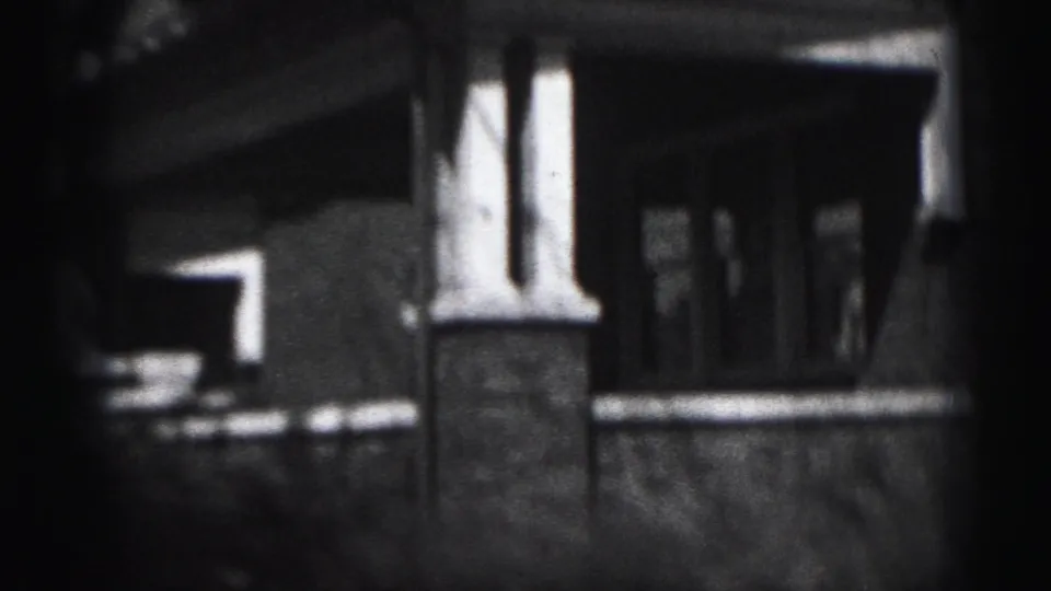 Close exterior view of a covered porch on the Harrisburg brick house, with columns, shadowed entry, and a low wall or railing.