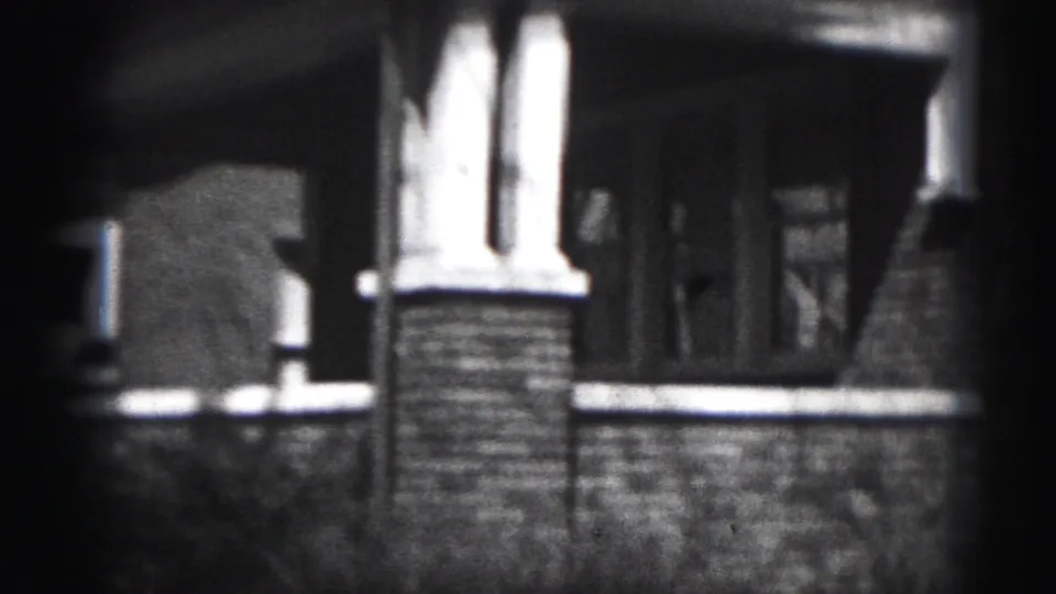 Soft 8mm frame of the house porch and front wall, showing a column, low masonry wall, and shadowed entry area.