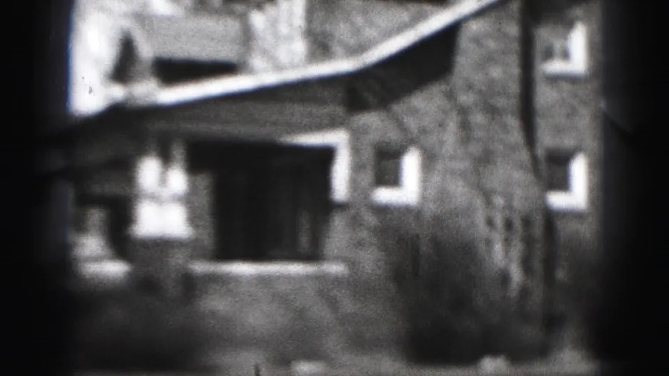 Black-and-white 8mm frame showing a Harrisburg house exterior with windows, porch area, and bare trees in 1975 home-movie footage.