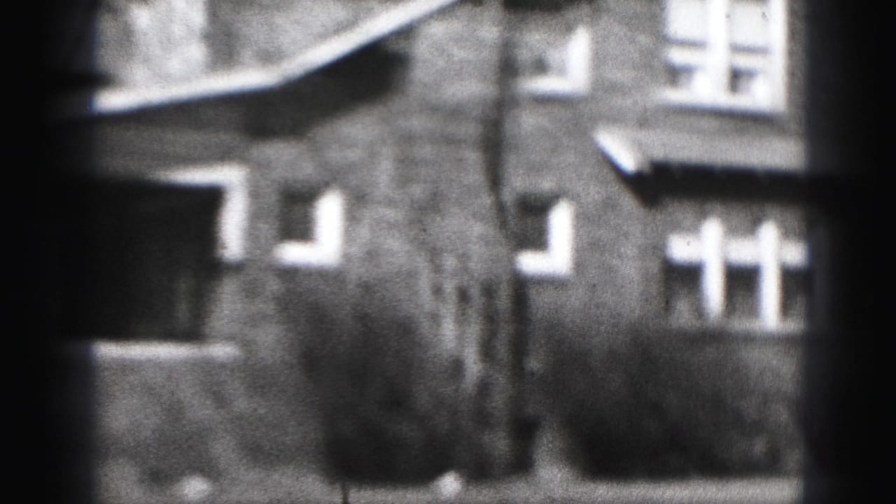 1975 Harrisburg home-movie frame showing brick residential houses, white windows, low shrubs, and soft 8mm blur.