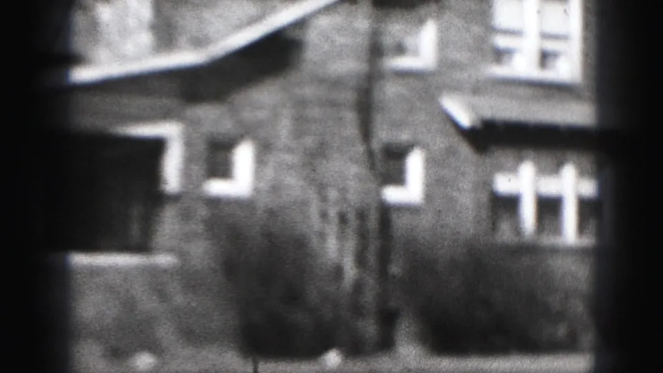 1975 Harrisburg home-movie frame showing brick residential houses, white windows, low shrubs, and soft 8mm blur.