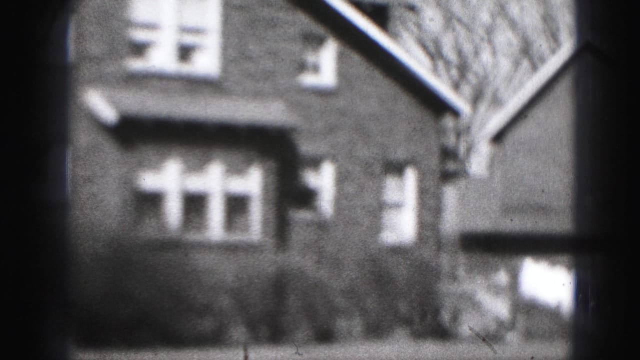 Brick house facade with white windows, shrubs, and a side building at right.