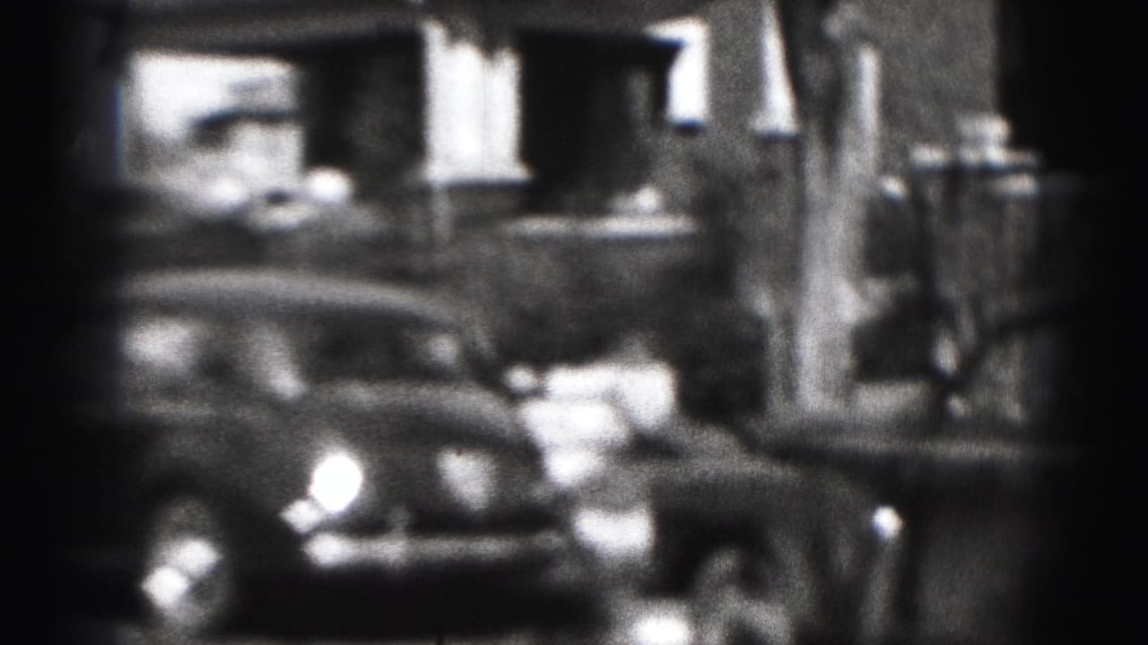 A parked car fills the foreground of a 1975 Harrisburg residential street view, with house fronts and shadows behind it.