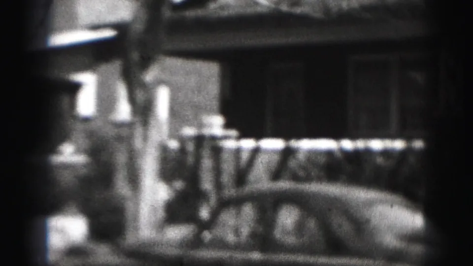 The camera dips toward porch railings and the top of a parked car on a Harrisburg residential block in 1975.