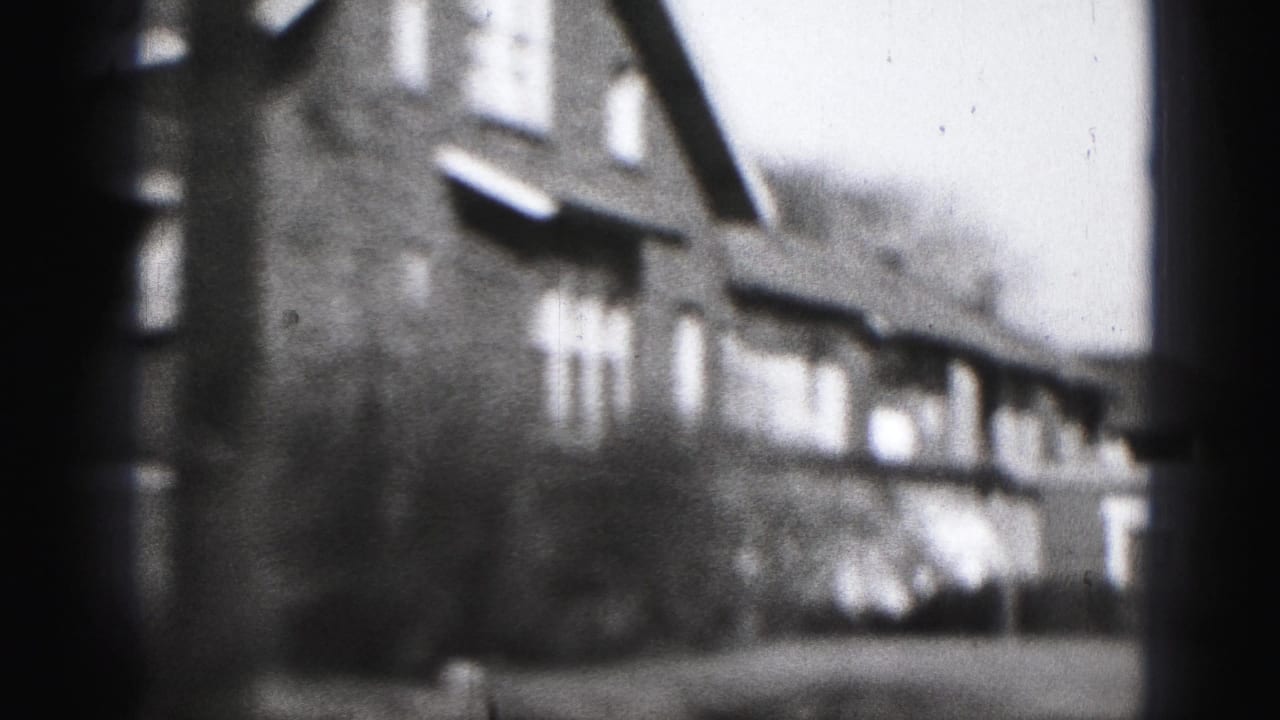Soft, grainy 8mm frame from Harrisburg showing a long residential facade with repeated windows and low vegetation in front.