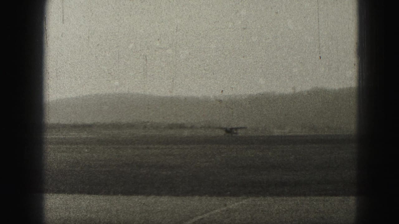 1975 Harrisburg airport frame showing a small propeller aircraft moving along a runway below hazy distant hills.