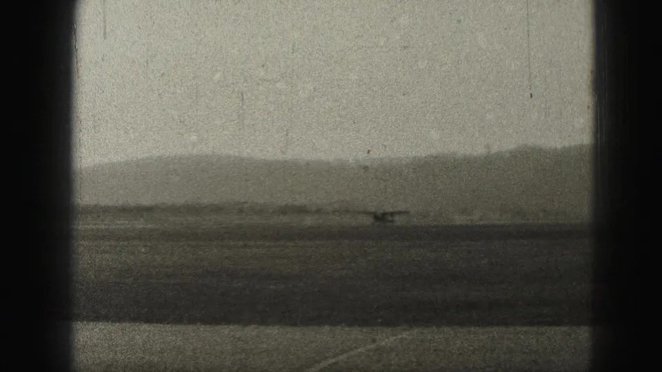 1975 Harrisburg airport frame showing a small propeller aircraft moving along a runway below hazy distant hills.