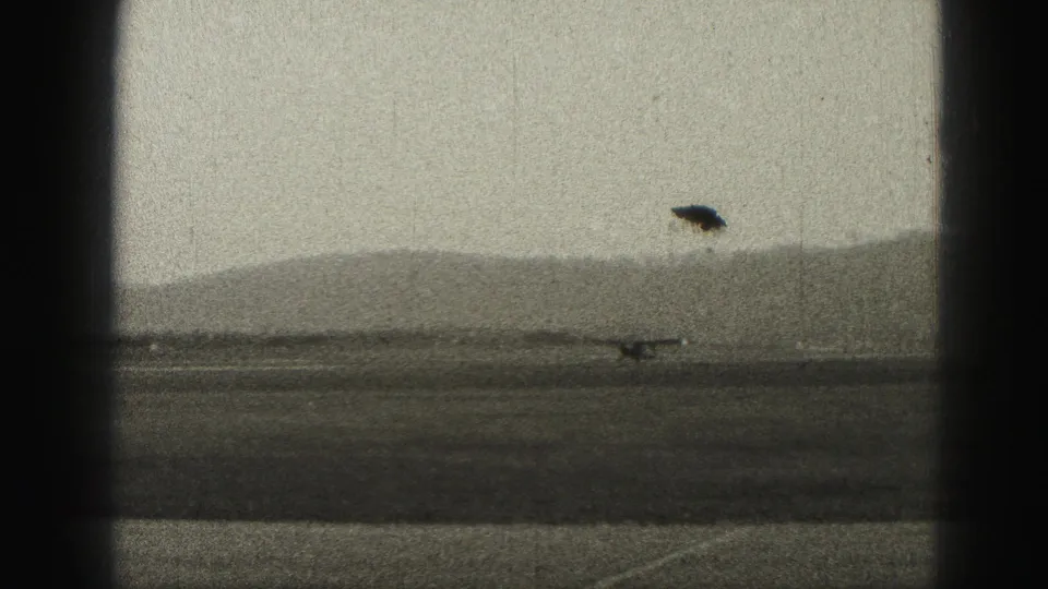 1975 Harrisburg airport frame with a small aircraft low on the runway and a dark film or exposure mark above the horizon.