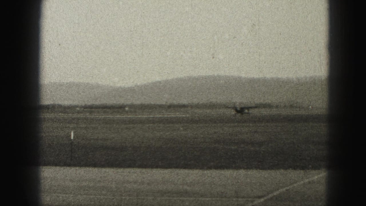 The aircraft continues along the runway at the Harrisburg-area airfield, with distant hills and heavy 8mm grain visible.