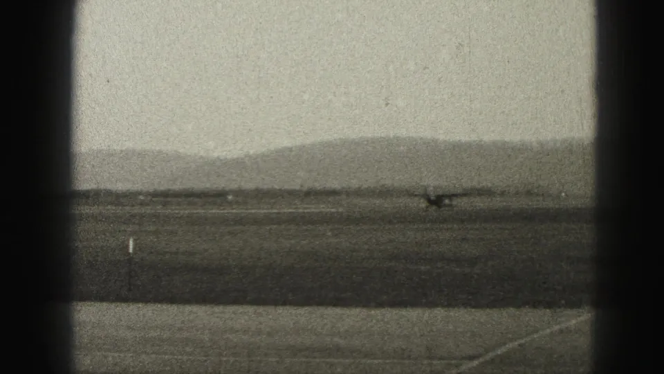 The aircraft continues along the runway at the Harrisburg-area airfield, with distant hills and heavy 8mm grain visible.