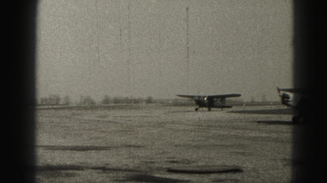 Small single-engine airplane on an open airfield, seen through dark vertical borders.