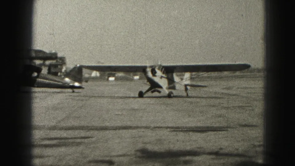 The single-engine airplane continues taxiing past a parked aircraft on the Harrisburg airport apron in 1975.