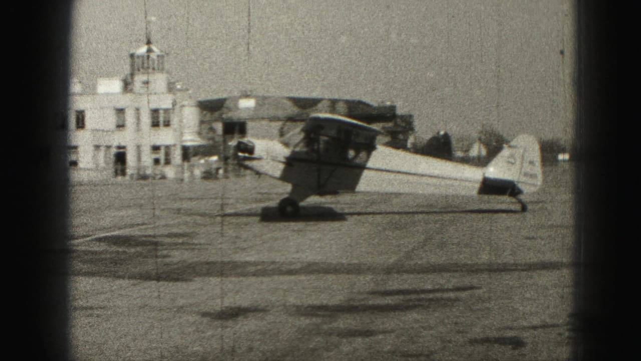 Small propeller plane parked on a runway near a low airport building.