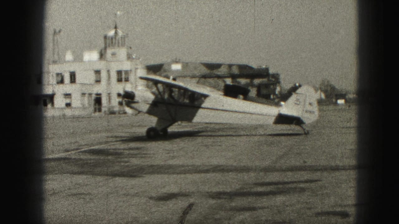Side view of a small propeller plane near a low airport building in Harrisburg, Pennsylvania, from 1975 8mm footage.