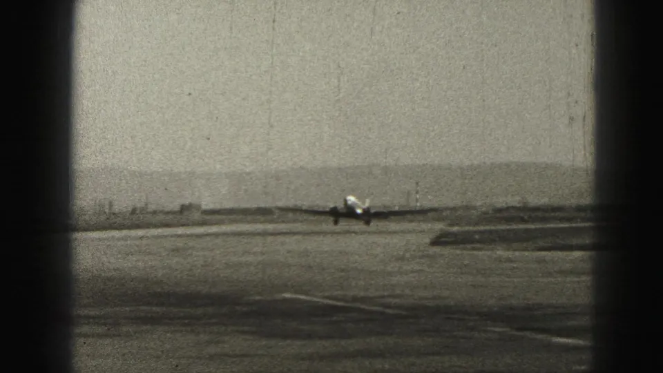 Distant view of a small propeller aircraft on a Harrisburg runway, with open airport grounds and pale sky visible.