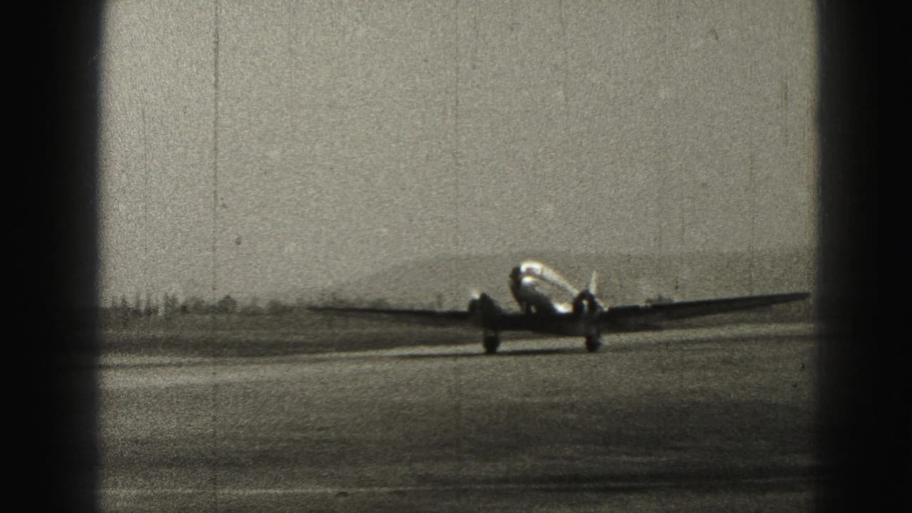 Passenger airplane taxiing closer across the runway with distant hills behind it.
