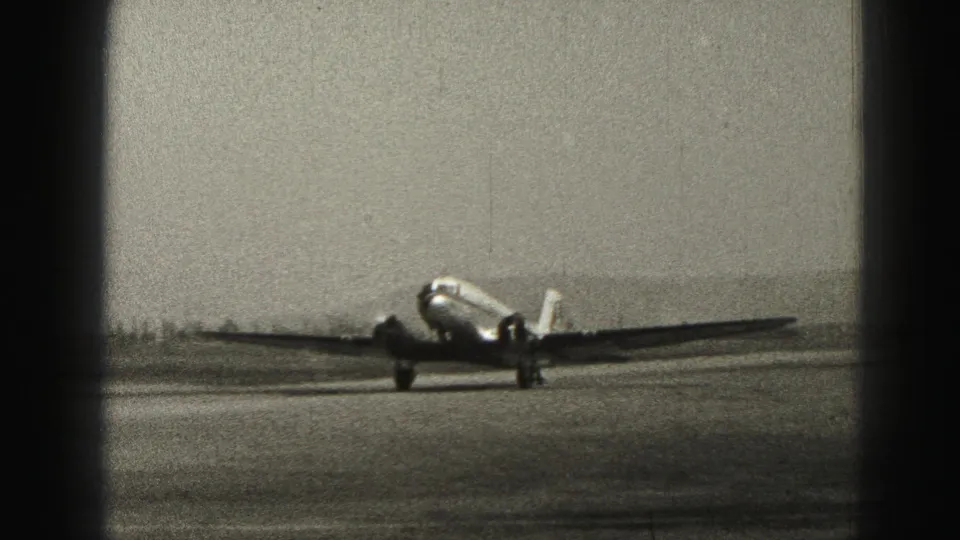 Closer 1975 Harrisburg runway view of a passenger airplane taxiing past, with grainy 8mm texture and dark frame borders.