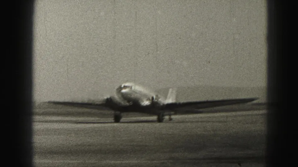 Grainy 8mm view of a passenger airplane taxiing past on a Harrisburg, Pennsylvania runway in 1975.