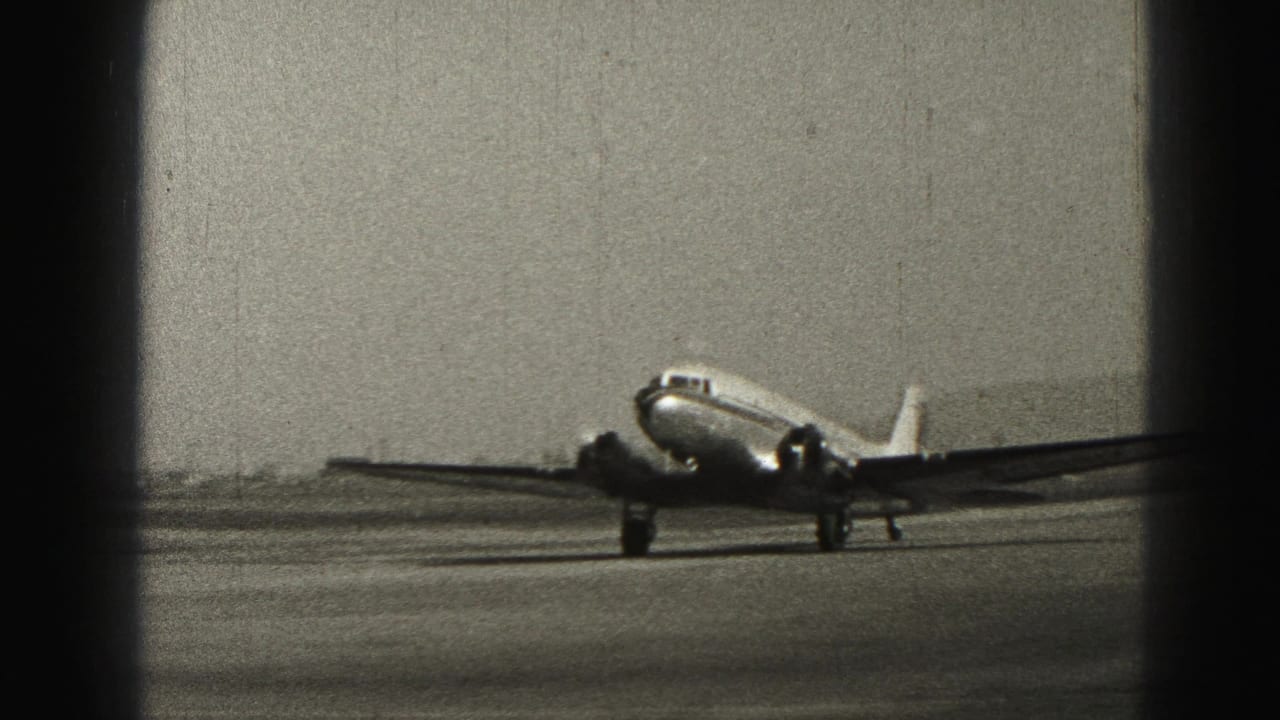 1975 Harrisburg home-movie frame showing a small propeller passenger aircraft taxiing across airport pavement.