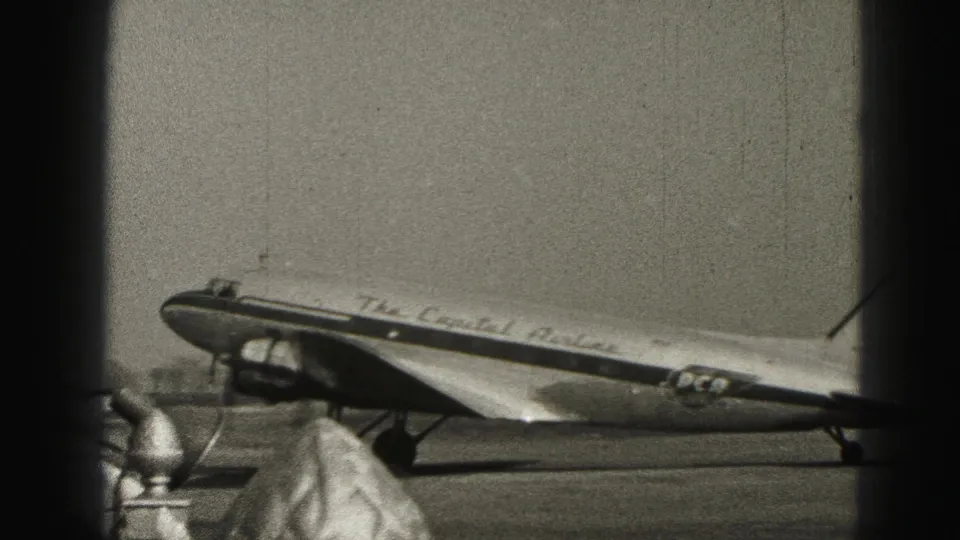 Capital Airlines marked propeller aircraft stands or taxis on the Harrisburg tarmac, partly obscured by terminal-window posts.