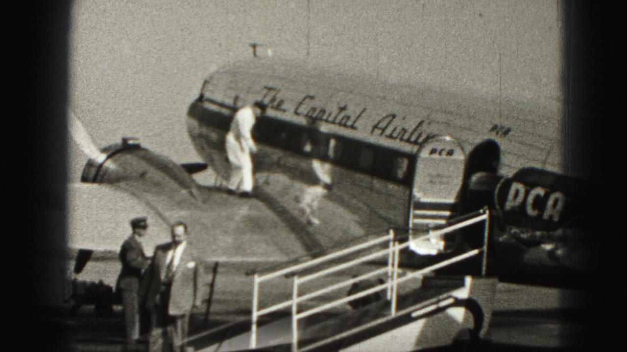 Passengers and crew near a marked aircraft with mobile stairs on an airport apron.