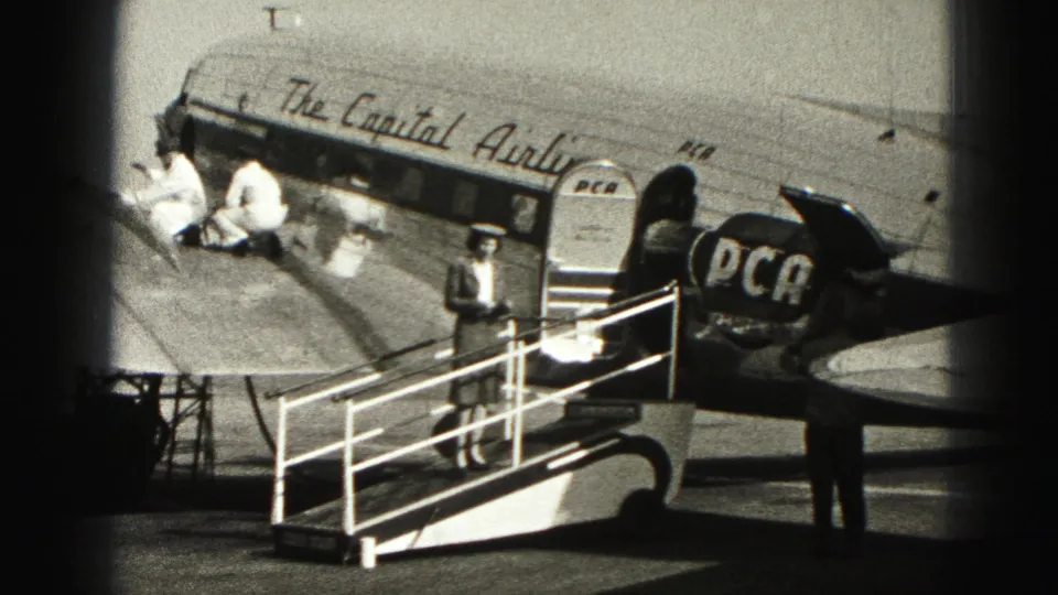 A uniformed attendant stands at the base of mobile stairs beside the Capital Airlines-marked aircraft in 1975 Harrisburg footage.