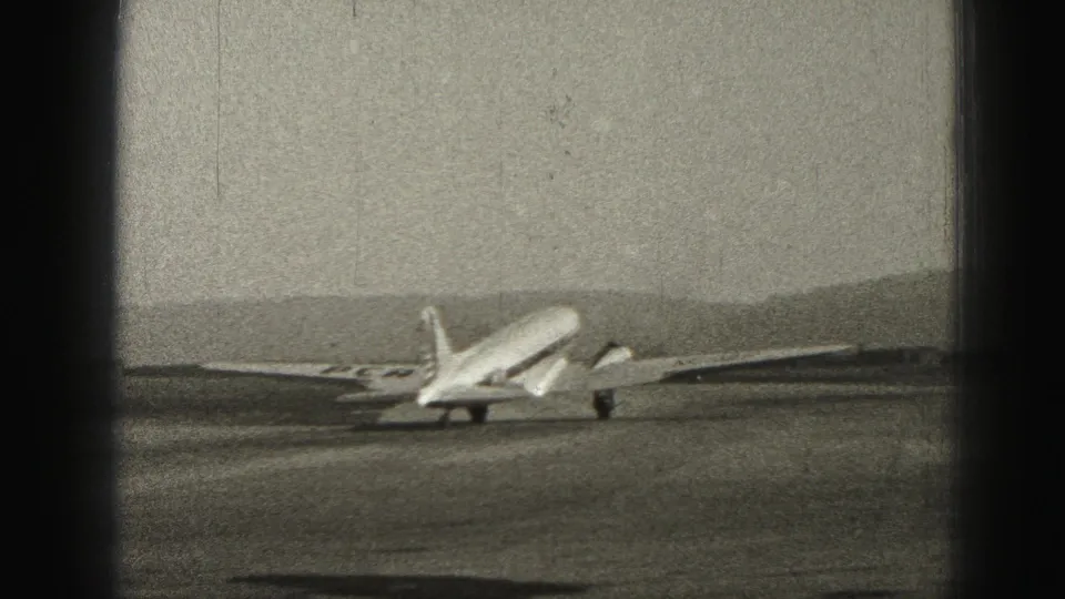The Harrisburg airport aircraft appears farther away on the runway, with tail and wing markings visible in soft 8mm focus.