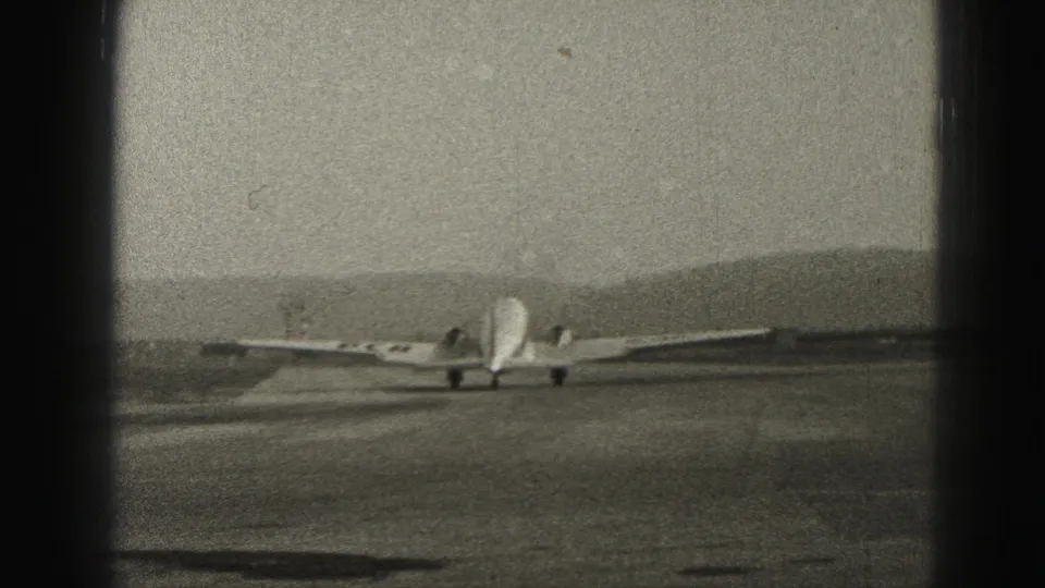 A small propeller aircraft recedes along the Harrisburg runway, framed by grain, scratches, and dark 8mm film borders.