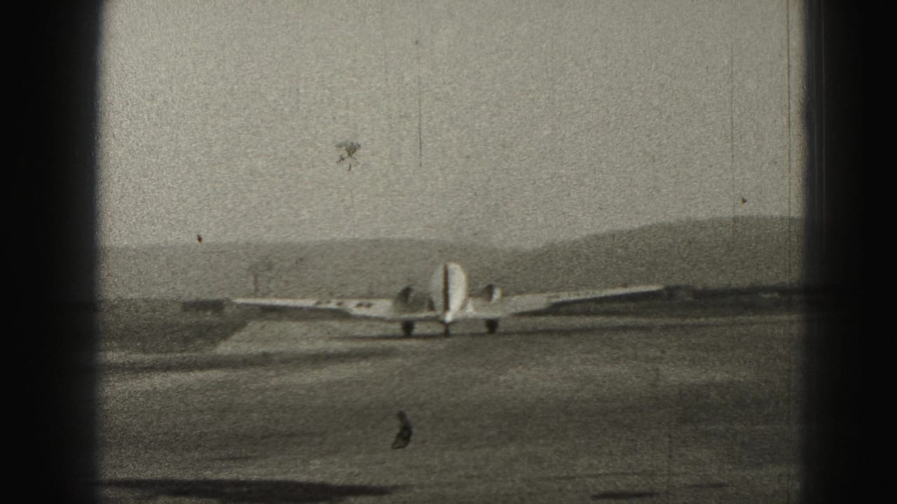 Small propeller plane on a runway with distant hills and dark film-frame edges.
