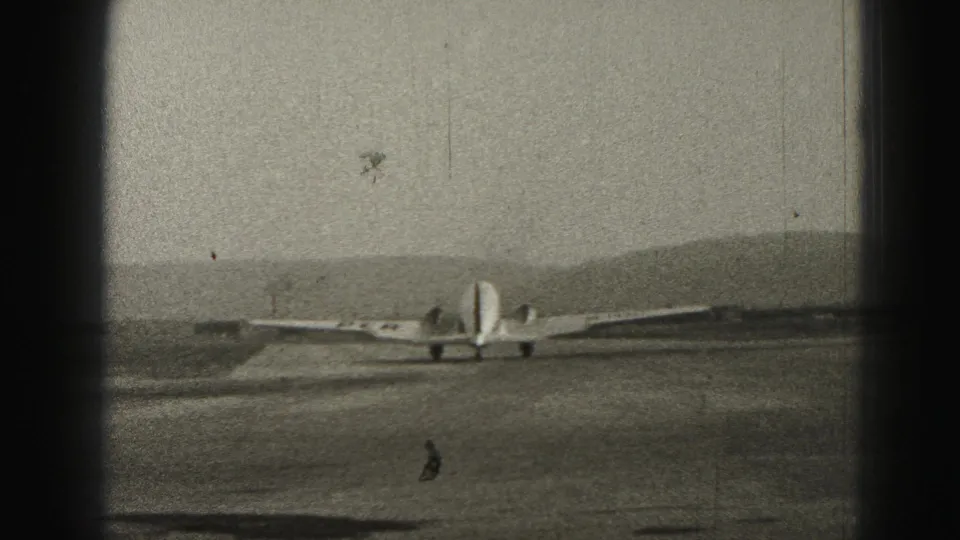 1975 Harrisburg-area home-movie frame showing a small propeller plane taxiing across a runway with hills in the background.