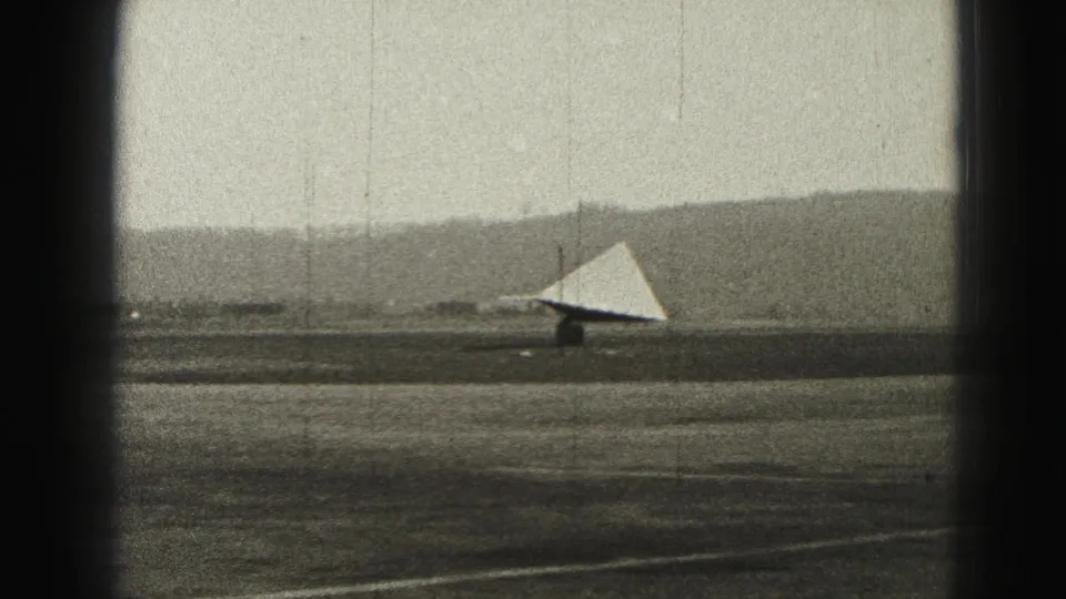 1975 Harrisburg-area runway view centered on a triangular wind indicator, with soft-focus hills and film wear visible.