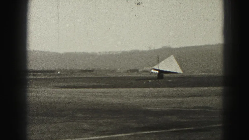 1975 Harrisburg-area home-movie frame showing the triangular wind indicator on the runway under a hazy sky.