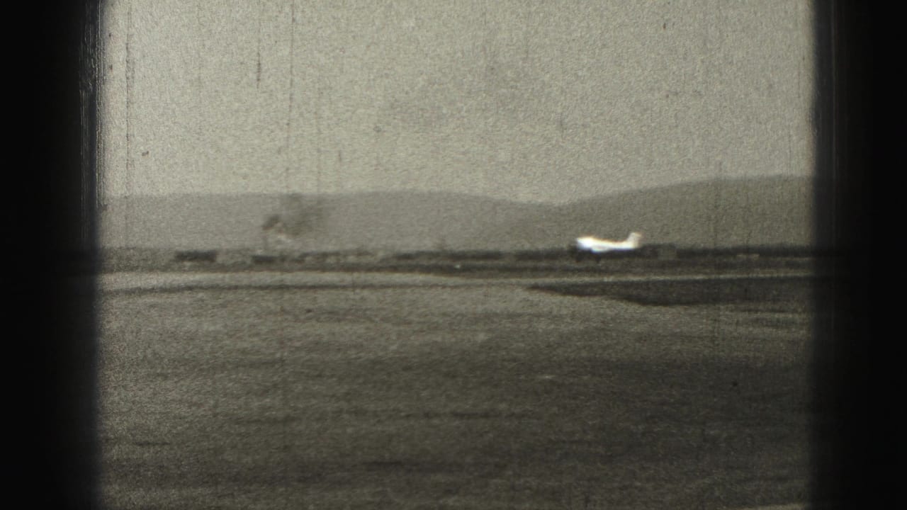 Small airplane on a runway seen through dark vertical framing bands with hazy hills behind it.