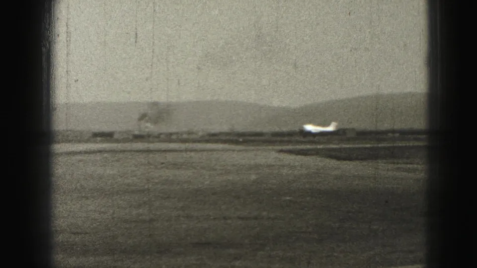 1975 Harrisburg-area 8mm frame showing a small plane low on the runway with distant hills and dark film or window edges.