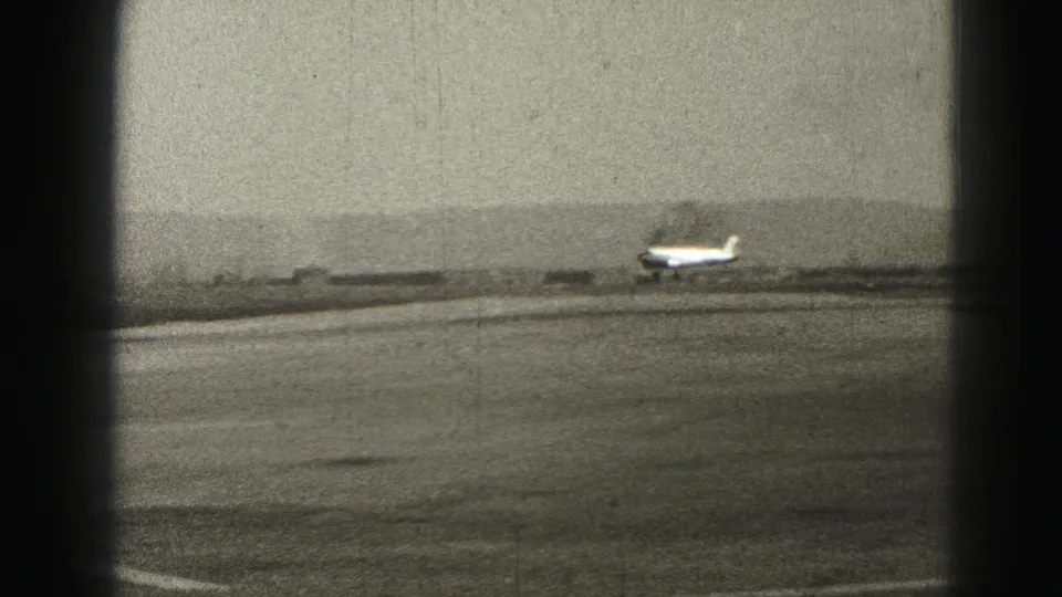 1975 Harrisburg-area 8mm frame of a small propeller plane just above the runway at a rural airport.