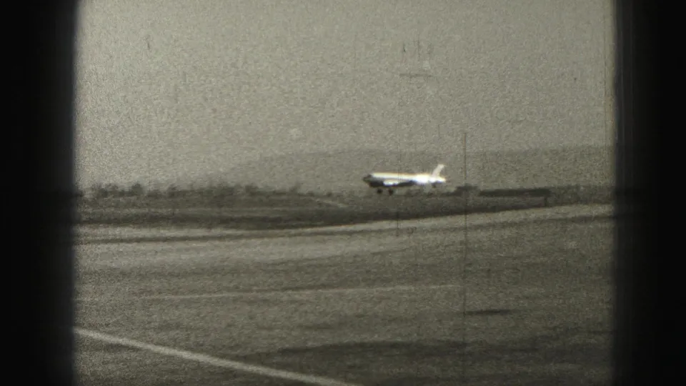 1975 Harrisburg-area 8mm frame showing a small plane airborne over the runway with landing gear still visible.