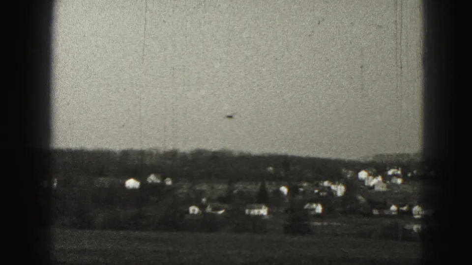 1975 Harrisburg-area 8mm frame of scattered distant houses and a treeline seen through dark window framing.