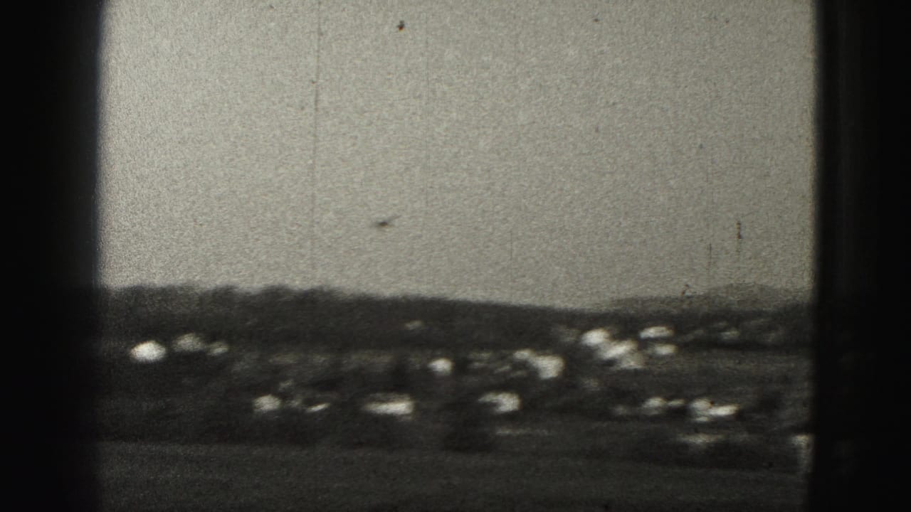 Small plane in the sky above distant suburban houses and wooded hills.