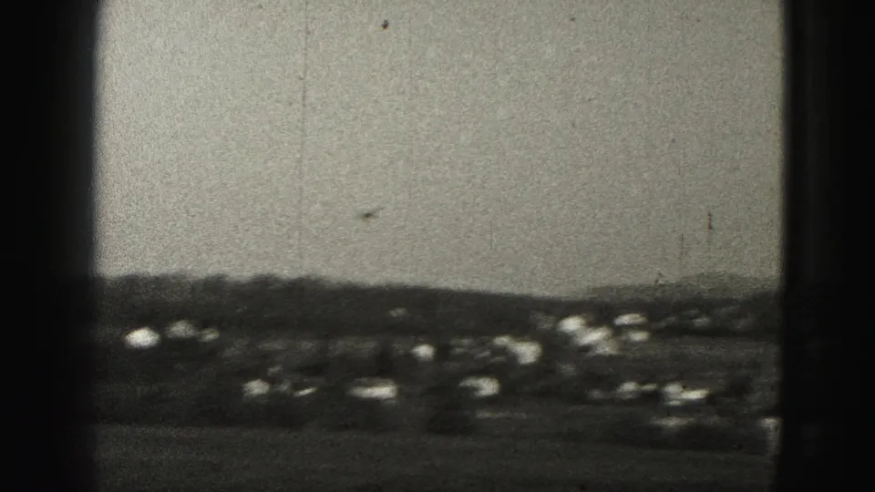 A small aircraft appears in the sky over distant homes and hills in 1975 Harrisburg home-movie footage.